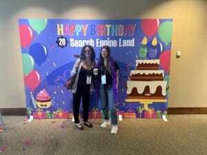 May and Olivia at SMX Boston conference by a Happy Birthday Search Engine Land sign